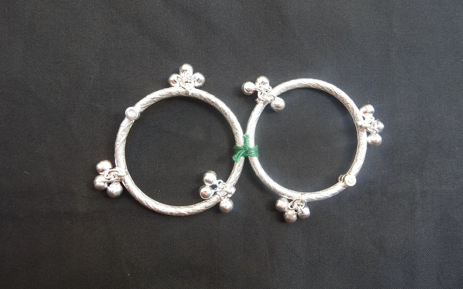 A pair of silver anklets with small bells on a dark cloth